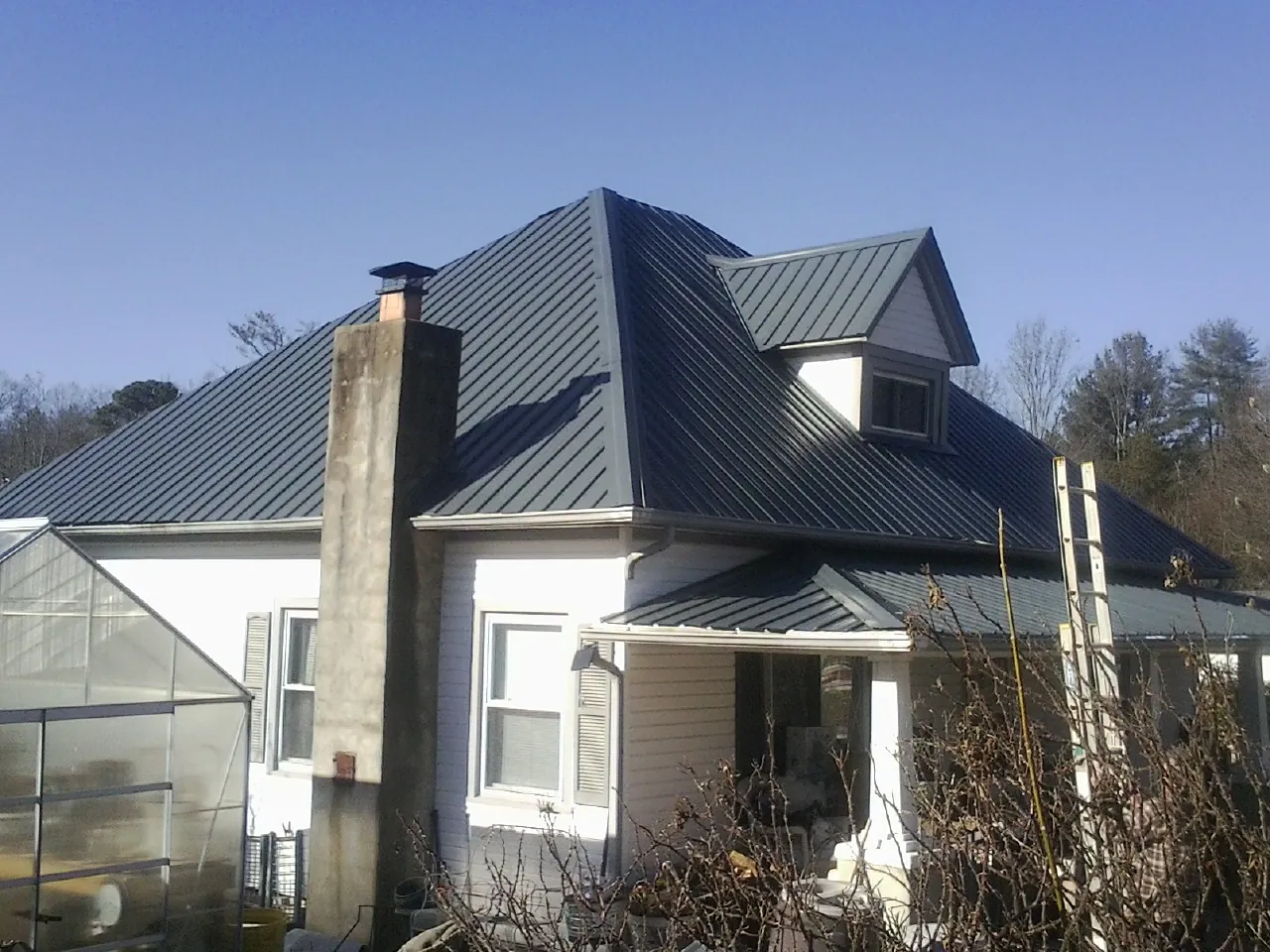 Dark blue standing seam metal roof on a white farmhouse with dormer — Slate & Tile Roof Repair by Roofing Brothers in Gallitzin