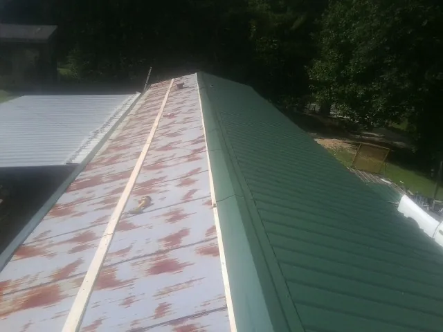 Old rusted panels beside newly installed green metal roofing — Wind Damage Roof Repair by Roofing Brothers in Gallitzin