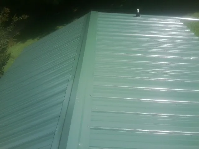 New green metal panels meeting at the ridge of a roof — Flat Roof Repair work by our crew in Gallitzin