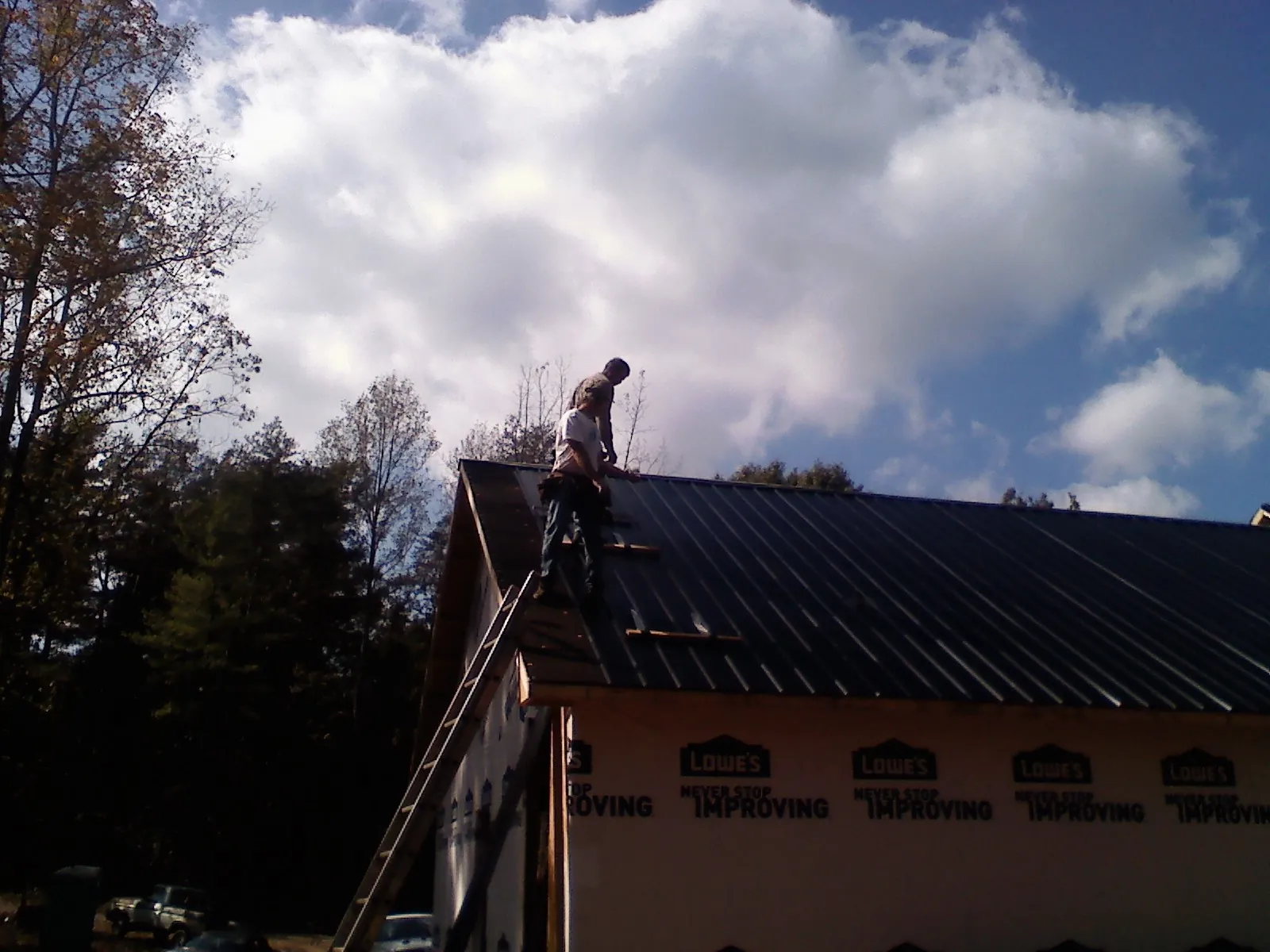 Roofer fastening dark metal panels high against a cloudy sky, from a Roof Inspection job in Gallitzin