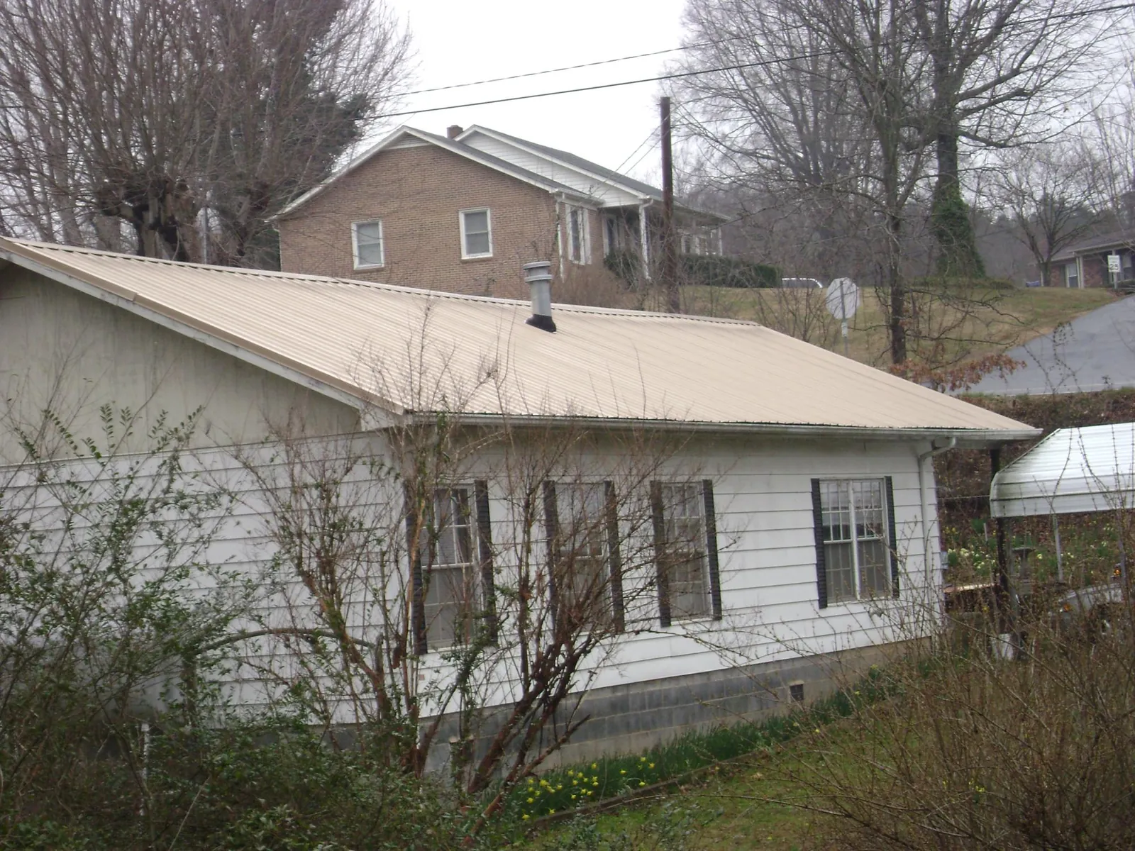 Tan metal roof on a white sided house set into a hillside — Commercial Roofing by Roofing Brothers in Gallitzin