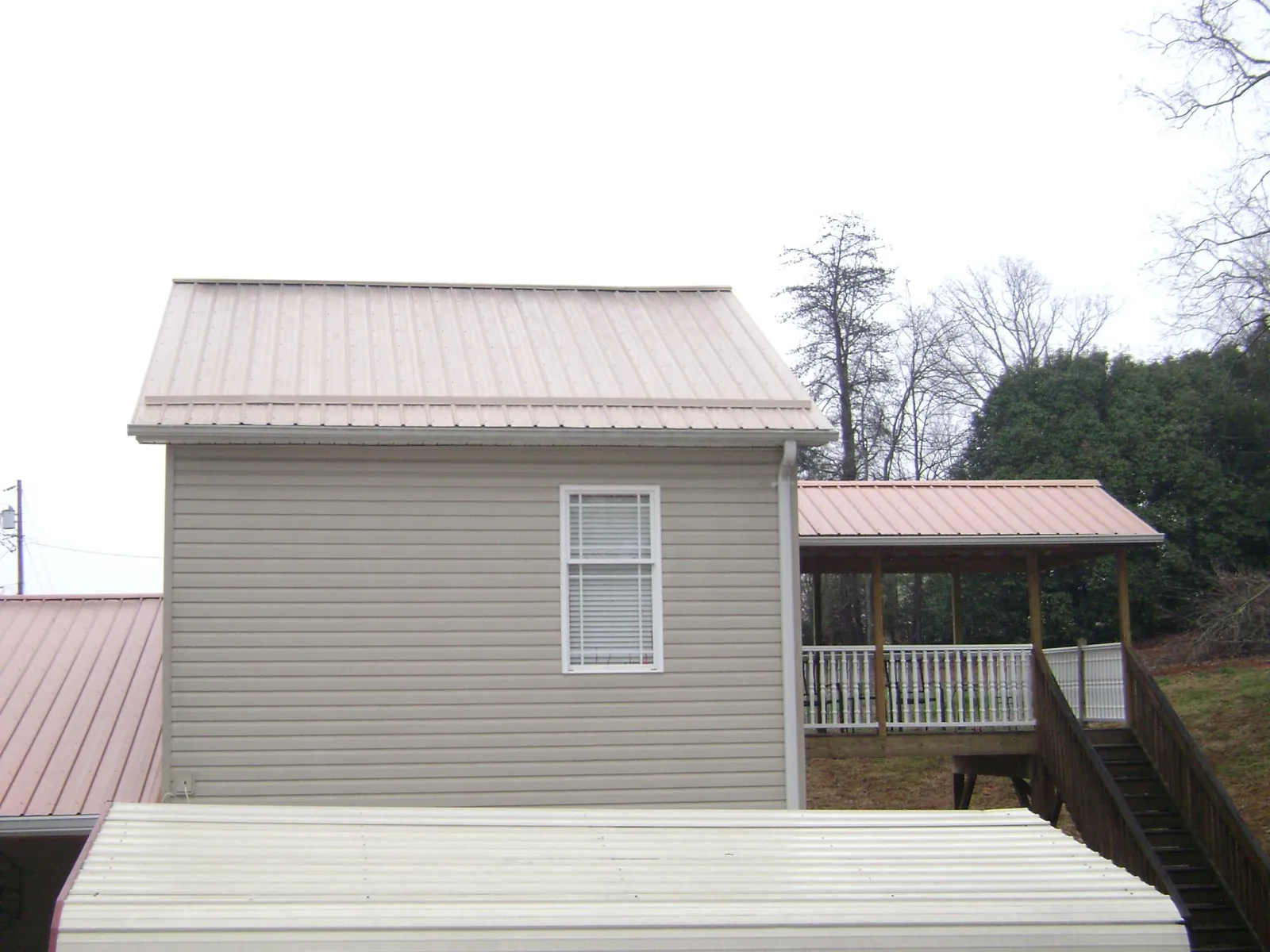Tan metal roofs on a two story addition and attached porch, from a Roof Replacement job in Gallitzin